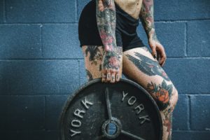 Tattooed woman holding weight plate. Work out at home.